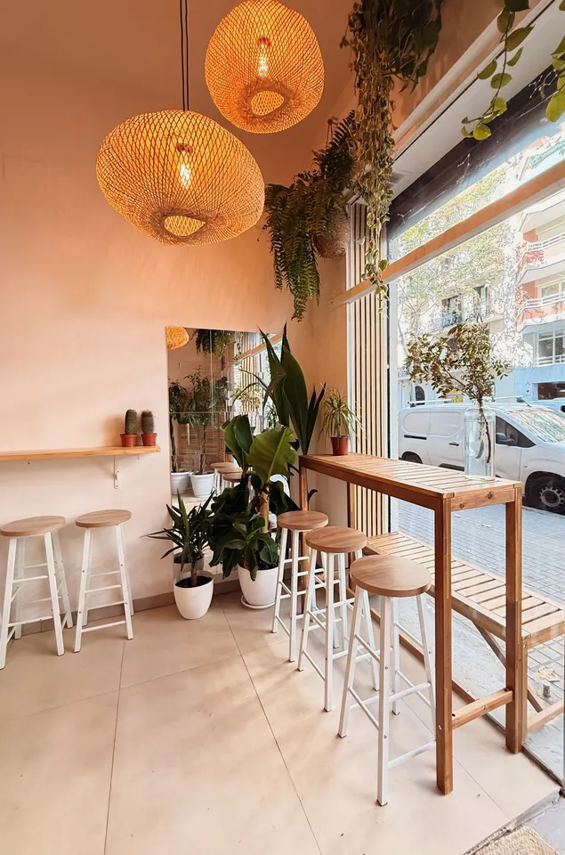 Interior de HOROSCOFFEE con lámparas de mimbre, plantas y taburetes junto al ventanal